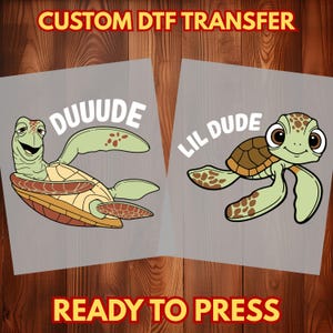 May include: Two DTF transfer sheets featuring cartoon sea turtles. One turtle says "DUUUDE" and the other says "LIL DUDE". The turtles are green, brown, and tan, with the text in white. The top text says "CUSTOM DTF TRANSFER" and the bottom text says "READY TO PRESS".