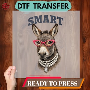 May include: DTF transfer with a donkey wearing pink glasses and a pearl necklace. The word "SMART" is above the donkey's head. The words "DTF TRANSFER" and "READY TO PRESS" are also displayed.