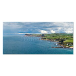 Può includere: Fotografia panoramica di un paesaggio costiero. L'immagine presenta una vasta distesa di oceano blu che incontra una costa frastagliata con campi verdi e scogliere sotto un cielo nuvoloso. Il testo "Robert McAlpin PHOTOGRAPHY" è visibile.