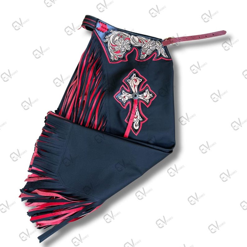 May include: Black leather chaps with red fringe and decorative stitching. The chaps feature a cross design with silver accents and floral embroidery. A leather strap is attached to the top.