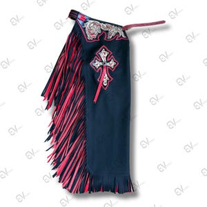 May include: Dark navy blue chaps with red and black fringe. The chaps feature a decorative cross design with red accents and floral embroidery. A leather strap is attached at the top.