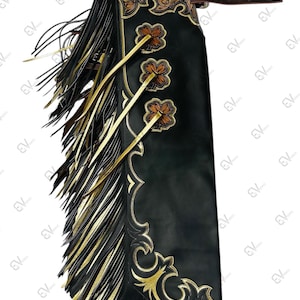 Peut inclure: Chaps en cuir noir avec des détails floraux dorés et marron et des franges. Les chaps présentent des motifs complexes sur le joug et des coutures décoratives. Des franges dorées et des lanières en cuir ajoutent des détails.