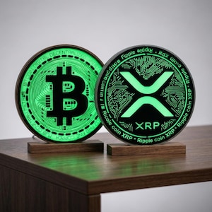May include: Two circular cryptocurrency signs, one featuring the Bitcoin logo and the other the XRP logo, both illuminated with a bright green light. Each sign is mounted on a small, rectangular wooden base, displaying intricate circuit board patterns.