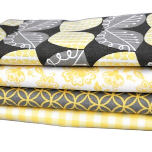May include: A stack of four folded fabric pieces with various patterns. The top fabric features a gray and yellow leaf design. The other fabrics have yellow floral, geometric, and gingham patterns. The fabrics are likely for sewing or crafting.
