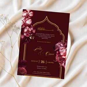 May include: Burgundy wedding invitation with gold accents and floral illustrations. The invitation features the names "Saia & Omar", date, time, and location. The design includes a decorative arch and floral arrangements.