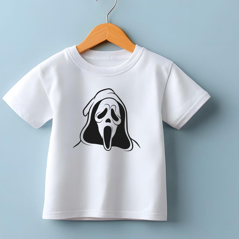 May include: White short-sleeved t-shirt featuring a black and white graphic of a Scream mask. The design is centered on the front of the shirt. The shirt is hanging on a wooden hanger against a light blue background.