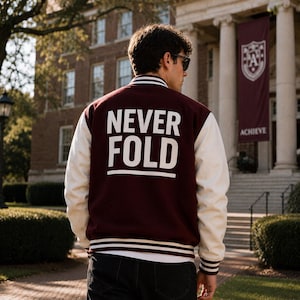Peut inclure: Une veste universitaire bordeaux avec des manches blanches et des bordures côtelées rayées blanches au col, aux poignets et à l'ourlet. Le dos présente le texte NEVER FOLD imprimé en grandes lettres capitales blanches sur le panneau bordeaux.