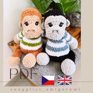 May include: Two handmade crochet monkey amigurumi dolls. One monkey is brown with a green and white striped shirt, the other is gray with a blue and white striped shirt. The dolls have black eyes and are sitting on a gray surface. The word "PDF" is in the image.