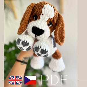 May include: A plush crochet beagle dog toy made with soft brown, white, and black yarn. The stuffed animal features long floppy ears, a white blaze on its face, a black nose, and white paws with dark gray paw pad details. Text reads PDF.