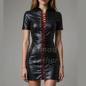 May include: Black leather dress with short sleeves and a high collar. The dress features a red lace-up detail down the front. The text "Nomad Leather" is printed on the dress. The dress is a mini-length.