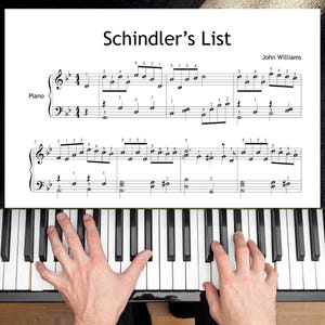 Puede incluir: Un teclado de piano con teclas blancas y negras. La partitura de "La lista de Schindler" de John Williams es visible encima del teclado. Las manos de una persona están tocando el piano.