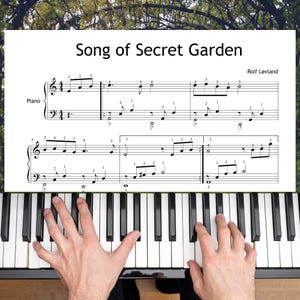 Può includere: Una tastiera di pianoforte con tasti neri e bianchi. Lo spartito intitolato "Song of Secret Garden" di Rolf Løvland è visibile sopra i tasti. Mani che suonano il pianoforte.