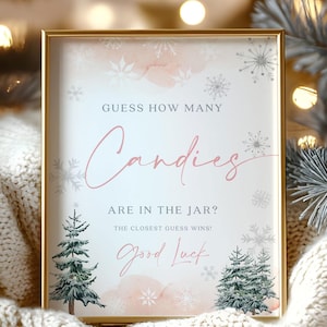 May include: A framed sign with gold trim, featuring the text "GUESS HOW MANY Candies ARE IN THE JAR? The closest guess wins! Good Luck." The sign has a light pink and white background with snowflakes and Christmas trees.