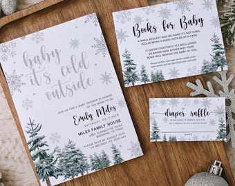 May include: A winter-themed baby shower invitation set on a wooden tray. The invitation reads "baby it's cold outside" with snowflake and pine tree graphics. Includes a "Books for Baby" card and a "diaper raffle" card.