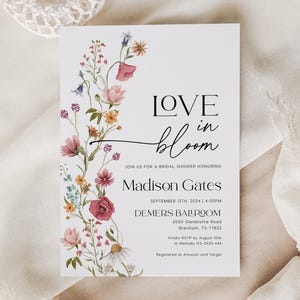 May include: A floral bridal shower invitation featuring the text "LOVE in bloom" and the name "Madison Gates". The invitation is adorned with a watercolour illustration of pink, red, and blue flowers.