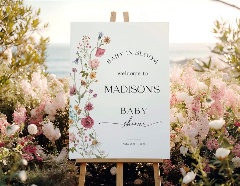 Editable “Baby in Bloom” baby shower welcome sign template with a vertical border of soft watercolor wildflowers in blush, burgundy, lavender, and yellow, paired with elegant script and serif fonts on a minimalist white background, customizable via Templett