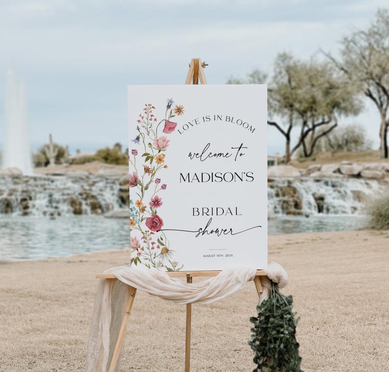 Editable “Love is in Bloom” bridal shower welcome sign template featuring a vertical border of soft watercolor wildflowers in pink, burgundy, lavender, and yellow, with modern script and serif fonts on a minimalist white background