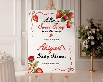 May include: A white sign on an easel with the text "A Berry Sweet Baby is on the way" and "Welcome to Abigail's Baby Shower August 12th, 2027". The sign is decorated with watercolor strawberries and red accents.