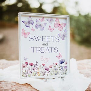 Puede incluir: Un cartel blanco con marco blanco y borde floral. El cartel dice "SWEETS and TREATS Enjoy!" con mariposas moradas y rosas sobre fondo blanco.