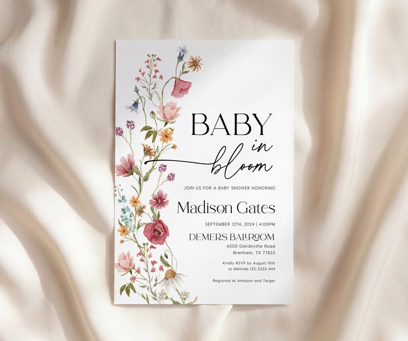 May include: A white baby shower invitation featuring floral designs. The text reads "BABY in bloom" with event details for Madison Gates, including the date, time, and location. The invitation is decorated with colorful flowers.
