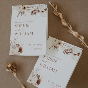 May include: Two wedding welcome signs with floral and botanical accents. The signs read "Welcome to the Wedding of Sophie and William" with the date 09.12.2023 and address details. Dried floral elements are arranged around the signs.