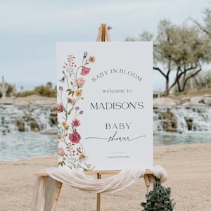 Editable “Baby in Bloom” baby shower welcome sign template with a vertical border of soft watercolor wildflowers in blush, burgundy, lavender, and yellow, paired with elegant script and serif fonts on a minimalist white background, customizable via Templett