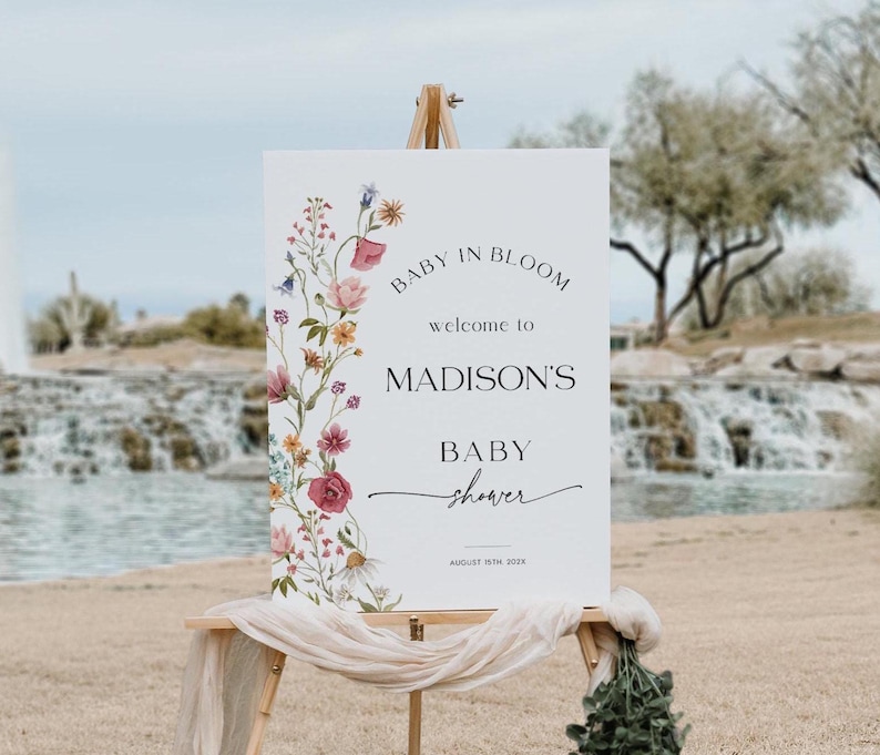 Editable “Baby in Bloom” baby shower welcome sign template with a vertical border of soft watercolor wildflowers in blush, burgundy, lavender, and yellow, paired with elegant script and serif fonts on a minimalist white background, customizable via Templett