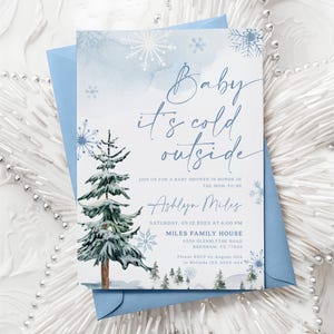 “Baby It’s Cold Outside” baby shower invitation with watercolor pine trees, scattered snowflakes, and elegant script on a soft winter background.