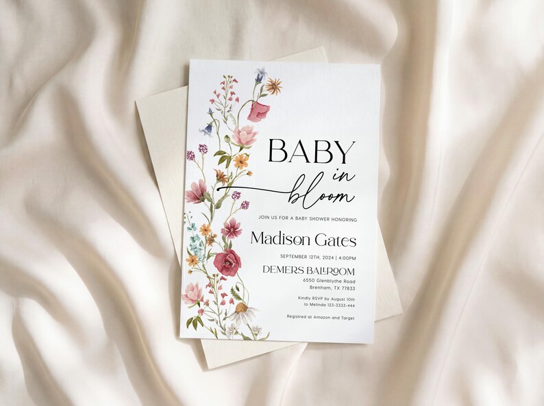 May include: A baby shower invitation featuring the words "BABY in bloom" in black script, adorned with watercolour flowers in pink, yellow, and blue. The invitation includes the name "Madison Gates" and event details.