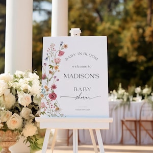 Editable “Baby in Bloom” baby shower welcome sign template with a vertical border of soft watercolor wildflowers in blush, burgundy, lavender, and yellow, paired with elegant script and serif fonts on a minimalist white background, customizable via Templett
