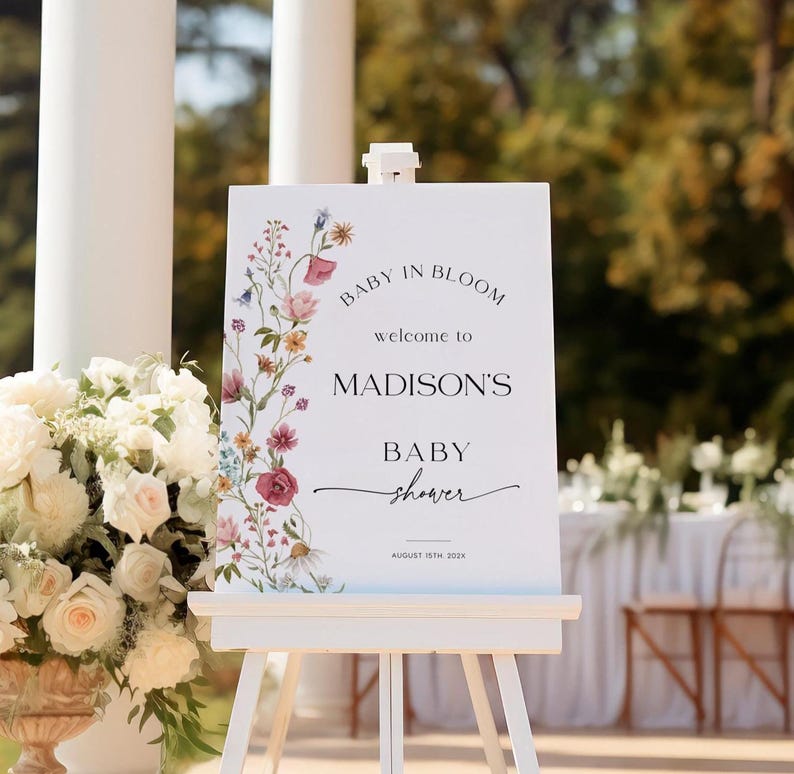Editable “Baby in Bloom” baby shower welcome sign template with a vertical border of soft watercolor wildflowers in blush, burgundy, lavender, and yellow, paired with elegant script and serif fonts on a minimalist white background, customizable via Templett