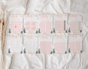 May include: A collection of ten baby shower game cards. Each card features a pink and white design with snowflake and pine tree illustrations. The cards include various game titles such as "Baby Bingo" and "Guess Who? Mommy or Daddy?"