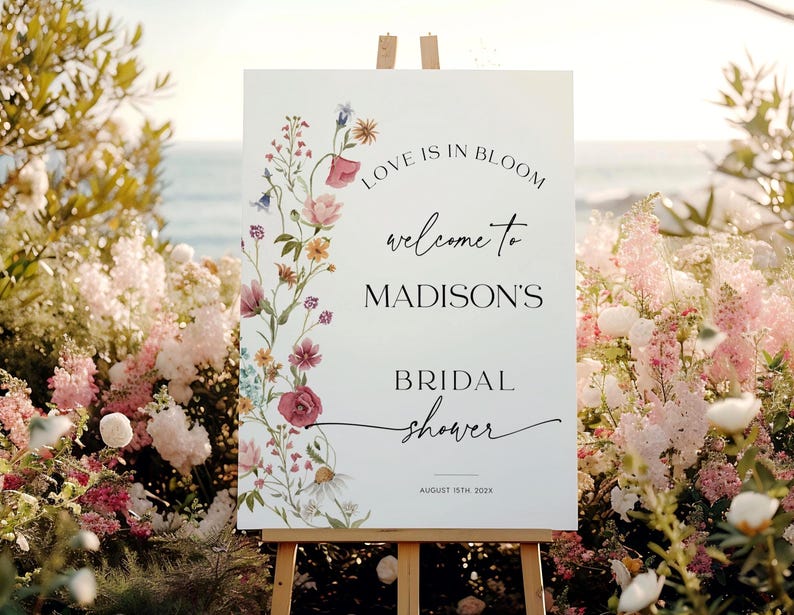 Editable “Love is in Bloom” bridal shower welcome sign template featuring a vertical border of soft watercolor wildflowers in pink, burgundy, lavender, and yellow, with modern script and serif fonts on a minimalist white background