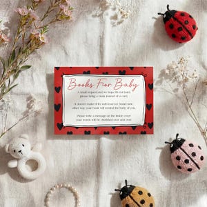 May include: A baby shower invitation card with the text "Books For Baby" in a red frame with black hearts. The image includes ladybug decorations, a white teddy bear rattle, and floral accents.