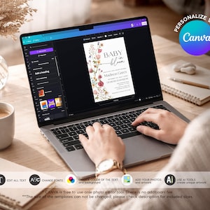 May include: A laptop screen showing a baby shower invitation design with floral elements and the words "BABY in bloom." The image includes editing tools and the Canva logo. A coffee cup, notepad, and pen are also in view.