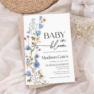 May include: A baby shower invitation with the words "BABY in bloom" in black script. The invitation is decorated with watercolor flowers in blue, yellow, and purple. The invitation includes the name Madison Gates and event details.