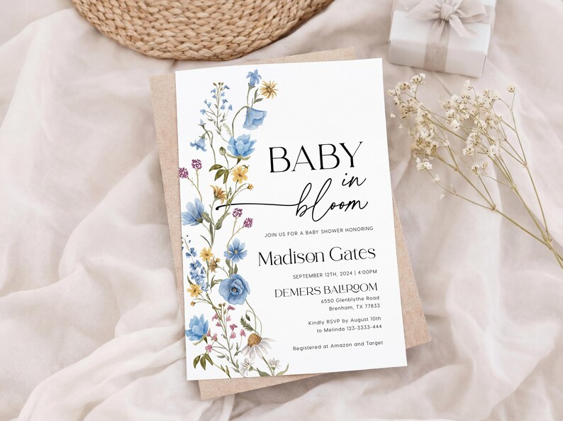 May include: A baby shower invitation with the words "BABY in bloom" in black script. The invitation is decorated with watercolor flowers in blue, yellow, and purple. The invitation includes the name Madison Gates and event details.