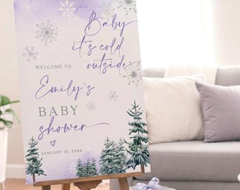 Może przedstawiać: Drewniany sztalug prezentuje znak baby shower z napisem "Baby it's cold outside" i "Emily's Baby Shower" w fioletowym skrypcie. Znak zawiera płatki śniegu i drzewa iglaste. Pudełka z prezentami i sofa w tle.