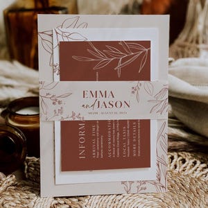 May include: A wedding invitation suite featuring a layered design with a neutral color palette. The suite includes a main invitation card, RSVP card, and details card, all adorned with botanical line art and the names "Emma and Jason".