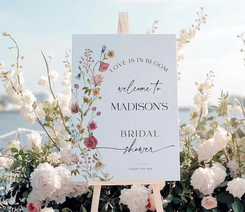 Editable “Love is in Bloom” bridal shower welcome sign template featuring a vertical border of soft watercolor wildflowers in pink, burgundy, lavender, and yellow, with modern script and serif fonts on a minimalist white background