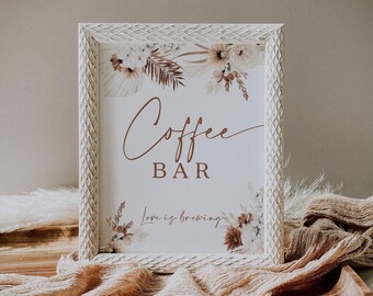 Könnte beinhalten: Ein weiß gerahmtes Schild mit den Worten "Coffee Bar" in brauner Schrift. Das Schild ist mit floralen Elementen in Braun- und Cremetönen verziert. Der Rahmen hat ein strukturiertes Muster. Der Satz "Love is brewing" steht darunter.