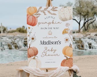 May include: A baby shower sign on an easel with a pumpkin theme. The sign reads "A Little Pumpkin is on the Way!" and "Welcome to Madison's Baby Shower." The sign is decorated with watercolor pumpkins and flowers.
