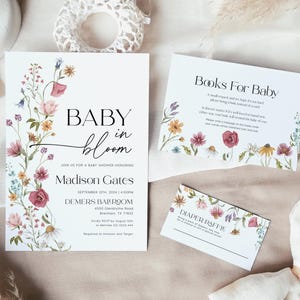 Op de afbeelding: Babydouche uitnodigingsset met bloemaccenten. De hoofduitnodiging luidt "Baby in Bloom" met evenementdetails. Extra kaarten zijn "Books For Baby" en een "Diaper Raffle" kaart. Het ontwerp toont aquarelbloemen in roze, geel en blauw.