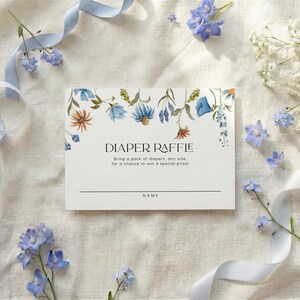 Matching white card featuring a hanging floral garland of blue and yellow wildflowers with "Diaper Raffle" text in the center.