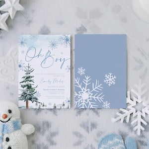 May include: Two rectangular invitation cards featuring a winter theme. The left card displays the text Oh Boy, a watercolor pine tree, and blue snowflakes. The right card is solid light blue with white snowflake illustrations on the corners.