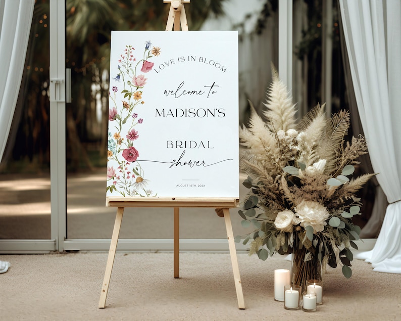 Editable “Love is in Bloom” bridal shower welcome sign template featuring a vertical border of soft watercolor wildflowers in pink, burgundy, lavender, and yellow, with modern script and serif fonts on a minimalist white background