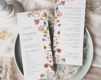 May include: Wedding ceremony programs with floral detailing. The programs are white with text and a floral border in pink, yellow, and blue. The programs are on a light green plate with decorative elements.