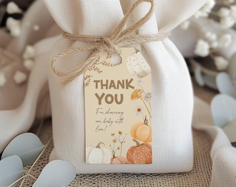May include: A beige fabric gift bag tied with twine, featuring a tag with the words "THANK YOU." The tag has watercolor illustrations of pumpkins and flowers. The text on the tag reads, "For showering our baby with love!"