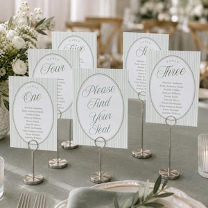 May include: A collection of white table seating cards with light green vertical stripes and oval borders, each held by a silver metal stand. The cards display table numbers, guest names, and the text Please Find Your Seat in script font.