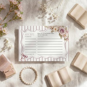 Puede incluir: Una tarjeta de recetas con detalles florales y el texto "Receta". La tarjeta está rodeada de elementos decorativos, incluyendo pequeños libros, una pulsera de perlas y flores. La tarjeta está diseñada para compartir recetas con la futura novia.